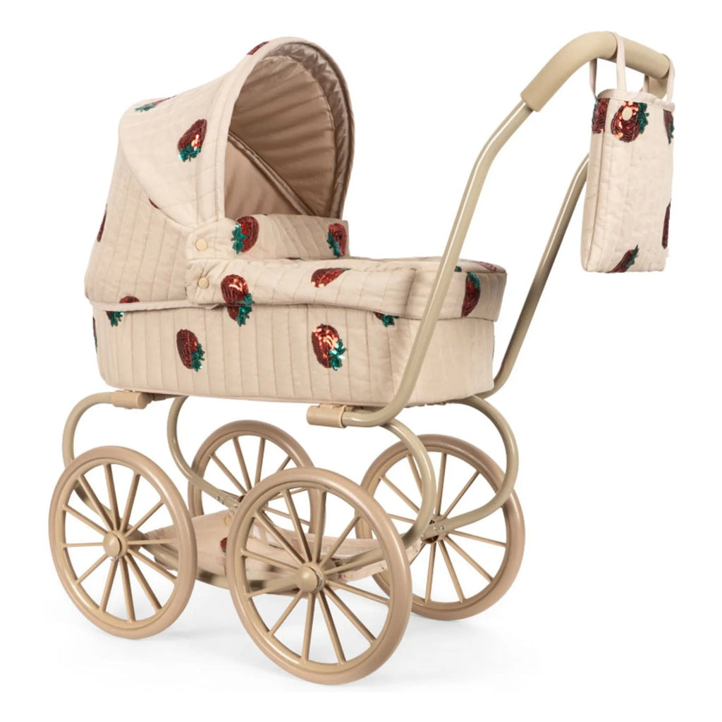 The Konges Sloejd Mini Doll Pram - Strawberry features beige quilted fabric, strawberry embroidery, four large wheels, and a matching hanging bag—an adorable and stylish toy stroller for creative pretend play.
