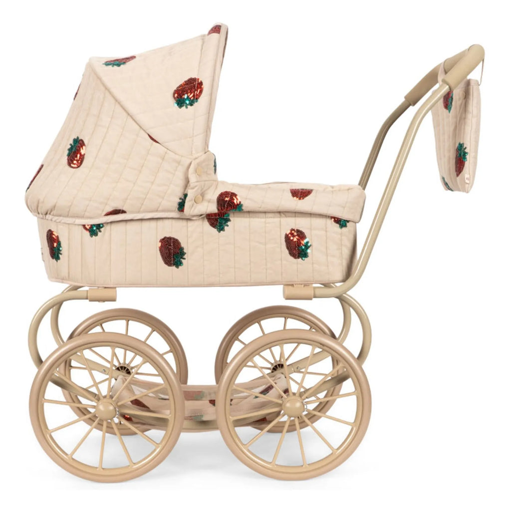 The Konges Sloejd Mini Doll Pram - Strawberry is a beige vintage-style pram with large wheels, a hood, and a bag, featuring red strawberry patterns on quilted fabric.