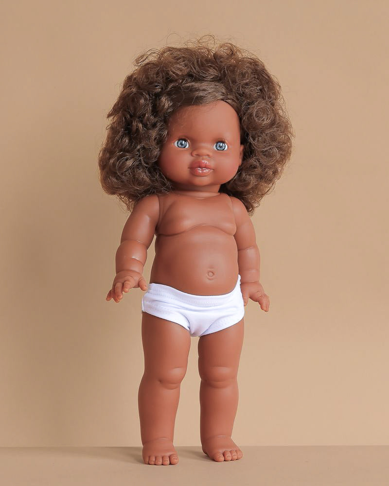 The Minikane Standing Doll (14") - Charlie features brown skin, curly brown hair, and blue eyes, shown upright in white underwear against a plain beige background. Clothing is sold separately. Made in Spain.