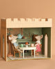 Two mouse figurines, wearing blue and pink outfits, are having a delightful Maileg Royal Tea Party at a small dining table in the furnished room of the dollhouse. The setting includes a teapot, cups, and cake set against green-ornate walls. While it's almost perfect, there is still a need to be cautious about potential choking hazards.