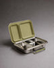 A stainless steel lunch box with two compartments and an olive handle is open, showing its matching olive-colored lid propped up behind it. The Haps Nordic eco-friendly food container is styled as a bento box and placed on a plain grey surface.