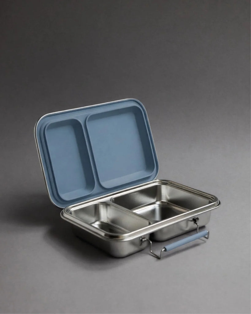 A Haps Nordic stainless steel lunch box with two compartments and an ocean blue lid is open on a gray background.