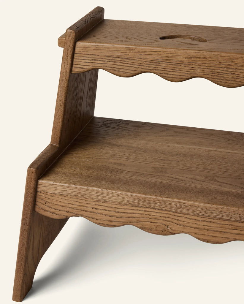 A close-up of the Häti at Home - Margot Step Stool, a kids' solid oak step stool with two steps, wavy decorative edges, a handle cutout on the top step, and a natural smooth finish.