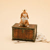 The Highness Hare Cake Topper - Final Sale (ships in one week) features a hand-painted crowned hare with a royal collar atop a wooden chest on a star-patterned cloth, perfect for birthday decorations.