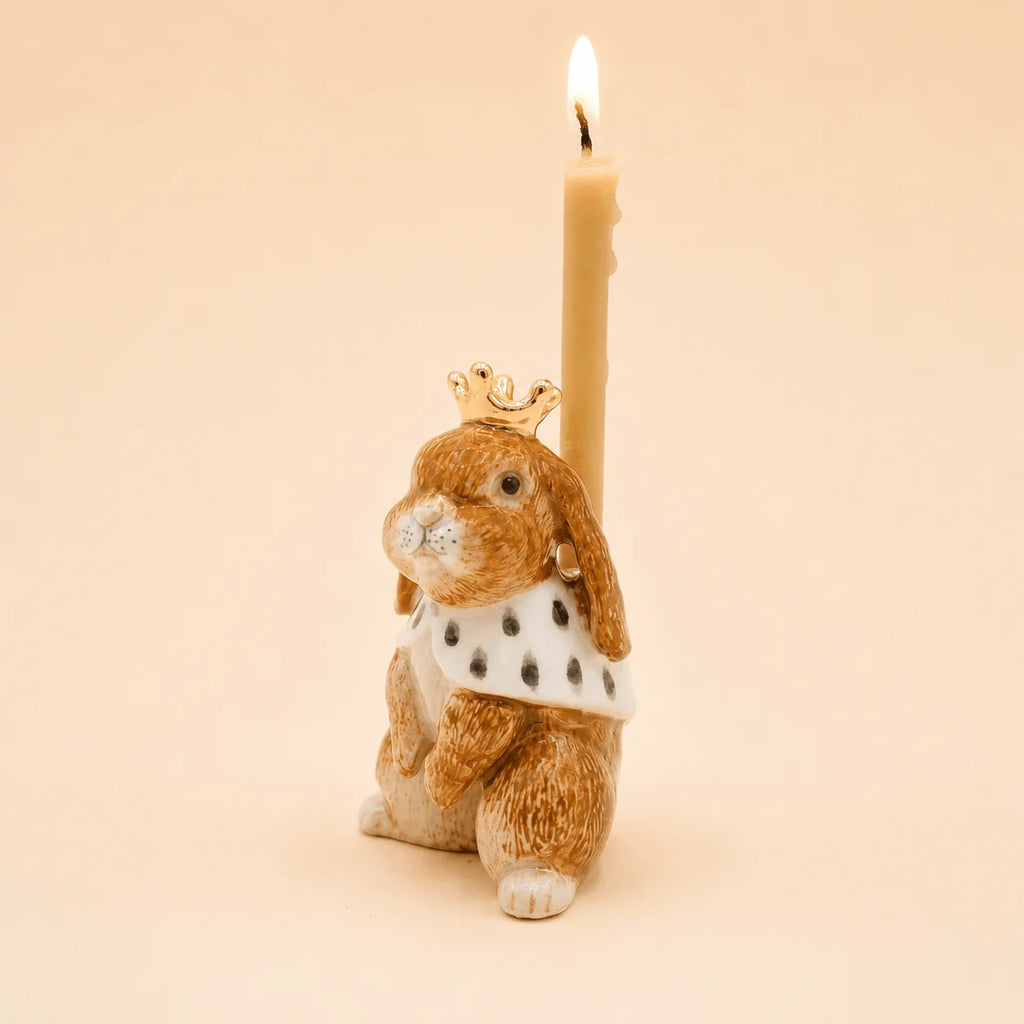 The Highness Hare Cake Topper - Final Sale (ships in one week) is a porcelain bunny figurine with a crown, cape, and lit candle on its back, shown against a solid light beige background.