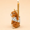 The Highness Hare Cake Topper - Final Sale (ships in one week) features a ceramic bunny with a gold crown and white spotted cape, holding a lit beige candle—a charming porcelain accent for your cake.