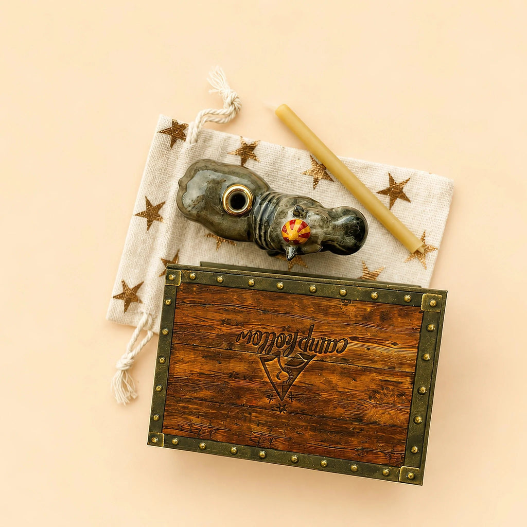 A collectible keepsake, the Hippo Cake Topper—featuring “Companion” scripted on its lid, a star-patterned cloth, a carved pipe, and a yellow candle—is beautifully arranged against a beige background, capturing the charm and elegance of an ornamental cake topper.