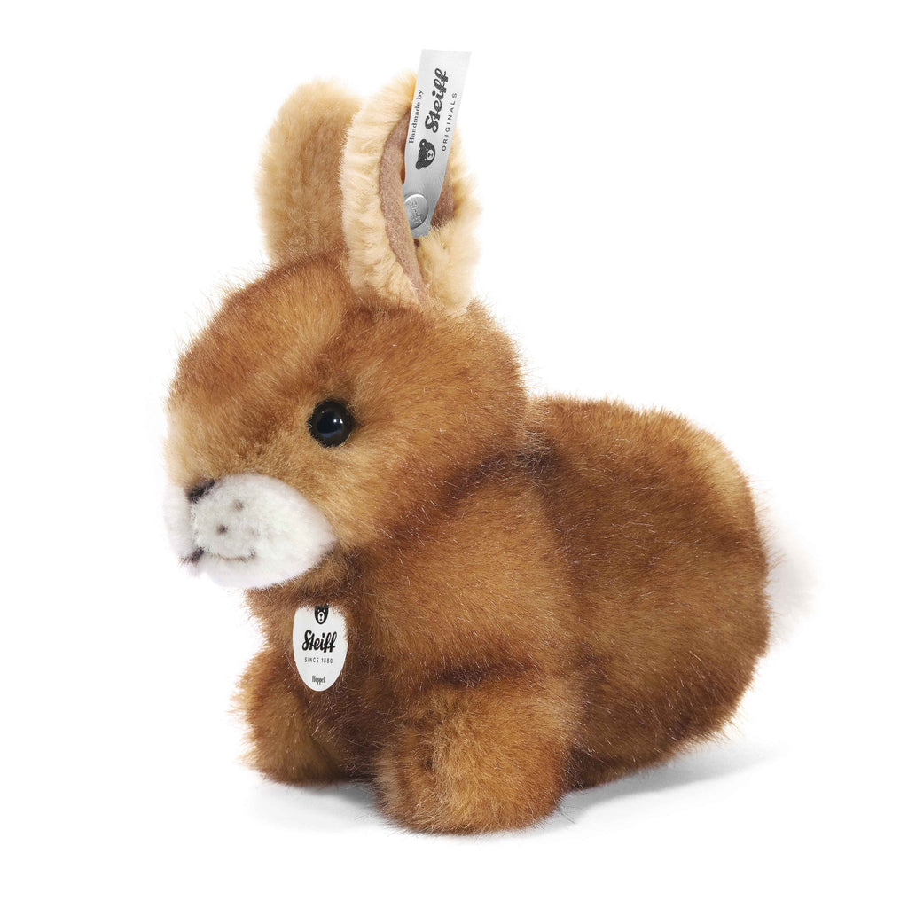 The Steiff Hoppel Rabbit is a soft brown plush bunny with upright ears, black eyes, and a white chest tag. Featuring a fabric "Steiff" tag on its ear, it’s machine washable, kid-friendly, and shown on a white background.