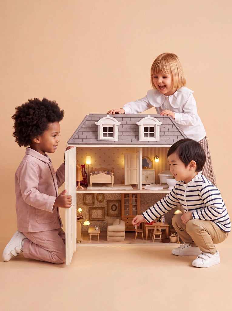 Three young children play together with the House of Hamptons — Little Forest Animals dollhouse, smiling and interacting with its miniature rooms and furniture against a beige background.