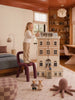 A young child stands on a purple chair, playing with the House of New York - The Six-Storey Giant: Fully Furnished Dollhouse With Lights in a cozy, stylish bedroom filled with toys, a bed, bookshelves, and soft natural lighting.