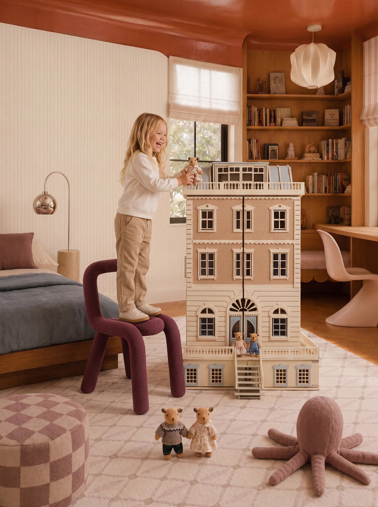 A young child stands on a purple chair, playing with the House of New York - The Six-Storey Giant: Fully Furnished Dollhouse With Lights in a cozy, stylish bedroom filled with toys, a bed, bookshelves, and soft natural lighting.