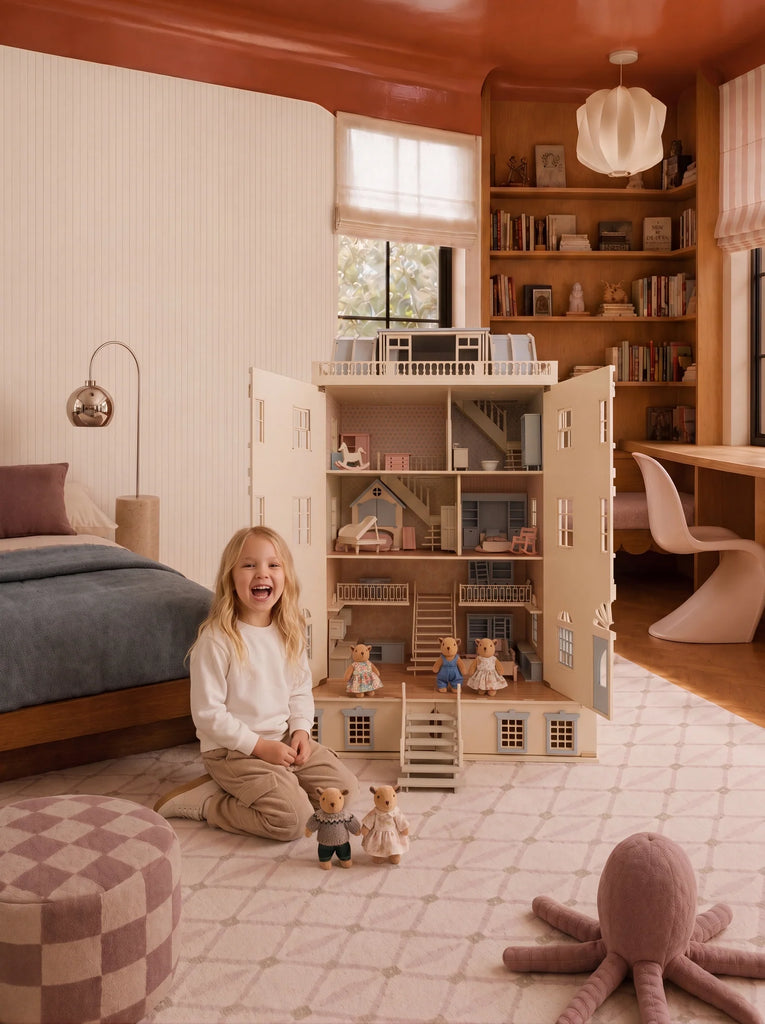 A young child sits and smiles in a cozy bedroom beside the Fully Furnished Dollhouse With Lights, House of New York - The Six-Storey Giant, complete with toy figures. The room features soft colors, a bed, bookshelves, and a plush octopus on the floor.