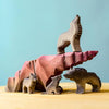 Four handcrafted Bumbu Handmade Wooden Howl Stone wolf figures are arranged on and around a multi-toned purple and pink rock-shaped platform, set against a light blue background atop a light wood surface—ideal for inspiring imaginative play.