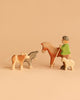The Handmade Holzwald Shepherd with Farm Animals Set features a shepherd with a staff riding a horse, alongside wooden cow, donkey, and lamb figures, all handcrafted and displayed against a plain beige background.