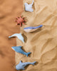 Various colorful ceramic sea creatures, including a starfish, whales, and a dolphin, artistically arranged on a sandy surface. These Handmade Wooden Stingrays are coated with child-safe paint.