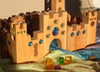 Bauspiel Large Fairytale Castle, 16-Piece Set wooden blocks featuring inset translucent star and circular gems, arranged on draped fabric with scattered colored translucent cubes for imaginative play.