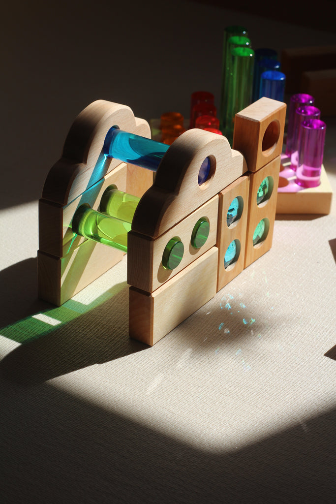 Bauspiel Luminous Pillars, 25-Piece Set wooden blocks with colorful translucent inserts arranged into a structure, casting light and color onto a surface.
