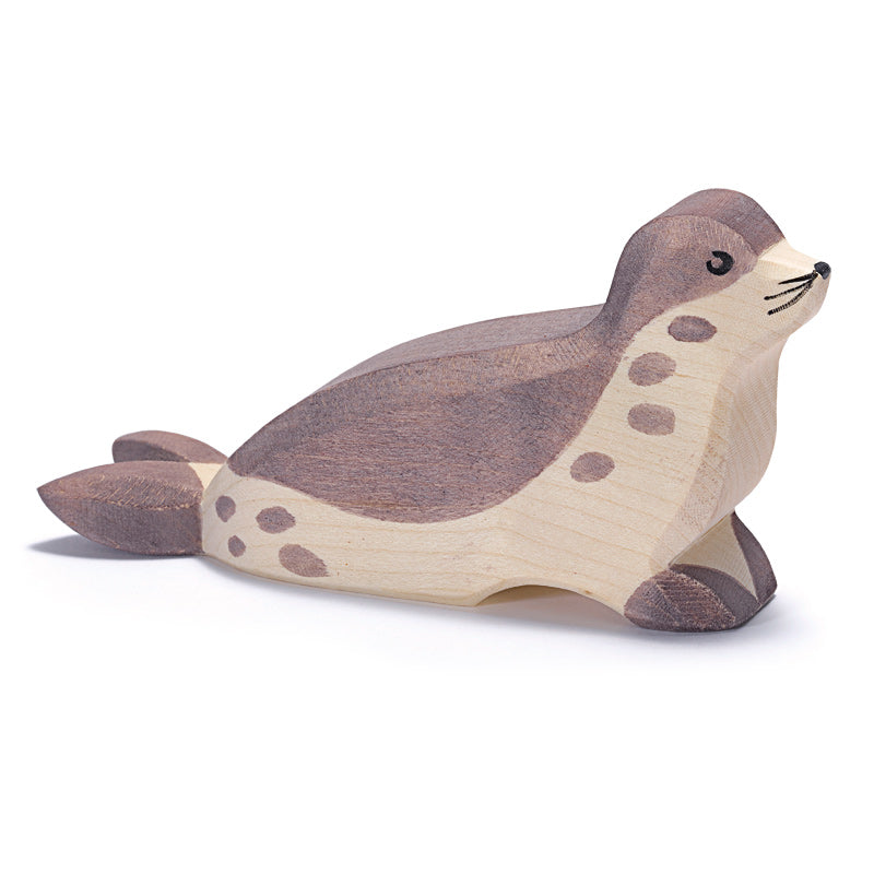 A Ostheimer Sea Lion - Head Low, handcrafted with a smooth finish, featuring a light and dark brown color scheme with darker spots and a simple, carved face. The sea lion is depicted lying down with flippers spread.
