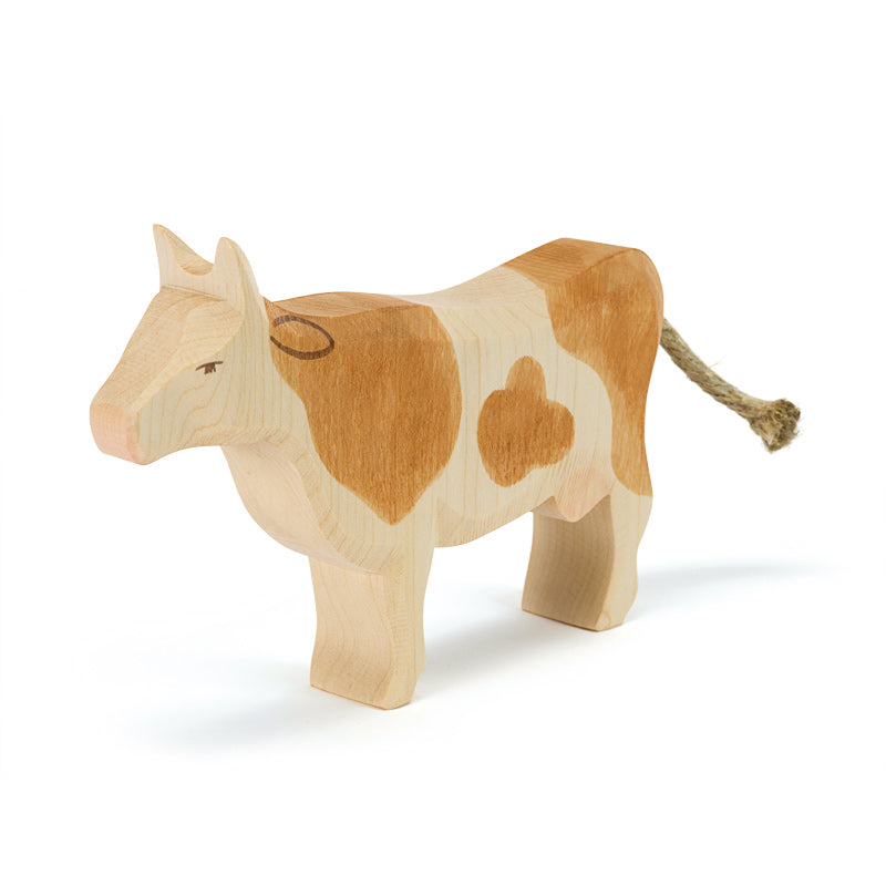 A Ostheimer Cow - Standing with natural wood and brown patches, standing on a white background. The cow has a simple, stylized design with a visible grain texture and a brown tail.
