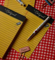 Two Class Notes Notepads with tear-off sheets, a pen, a pencil, a pink eraser, and paper clips are arranged on a red and white checkered tablecloth.