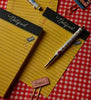 Two Class Notes Notepads with tear-off sheets, a pen, a pencil, a pink eraser, and paper clips are arranged on a red and white checkered tablecloth.