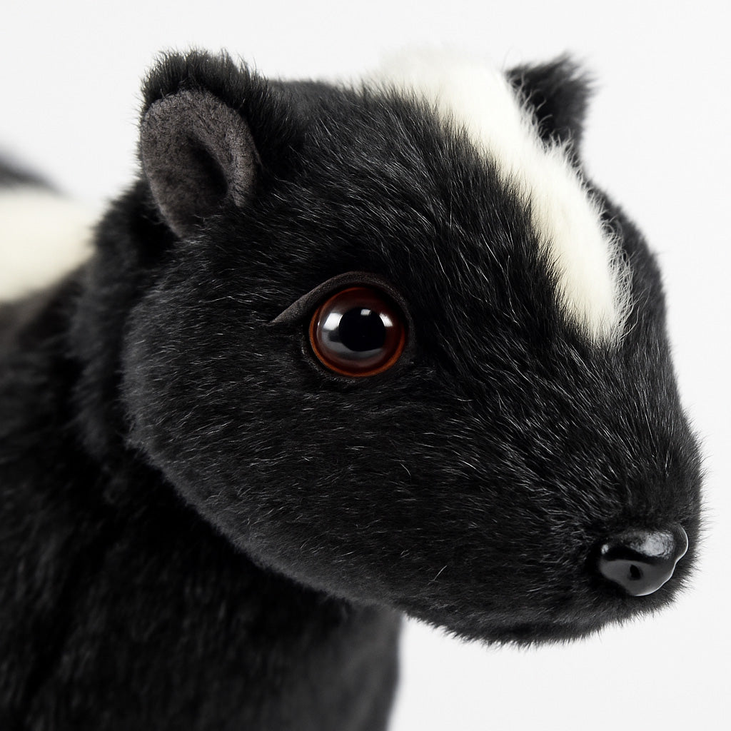 Close-up of a Skunk Stuffed Animal plush toy featuring black fur, a white head stripe, round dark eyes, and a shiny black nose against a plain white background.