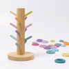 The Grimm's Pastel Sorting Helper for Building Rings is a wooden ring toss game crafted from non-toxic alder-wood, featuring a vertical pole and vibrant pegs. Pastel-colored rings are scattered around the base on a white surface. This playful design, intended for children, showcases bright hues and simplicity.