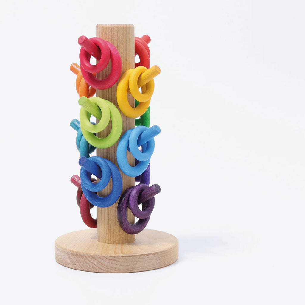 The Grimm's Sorting Helper for Building Rings - Rainbow is a wooden vertical stand with colorful rings on red, orange, yellow, green, blue, and purple dowels arranged in a gradient—perfect for fun sorting games.