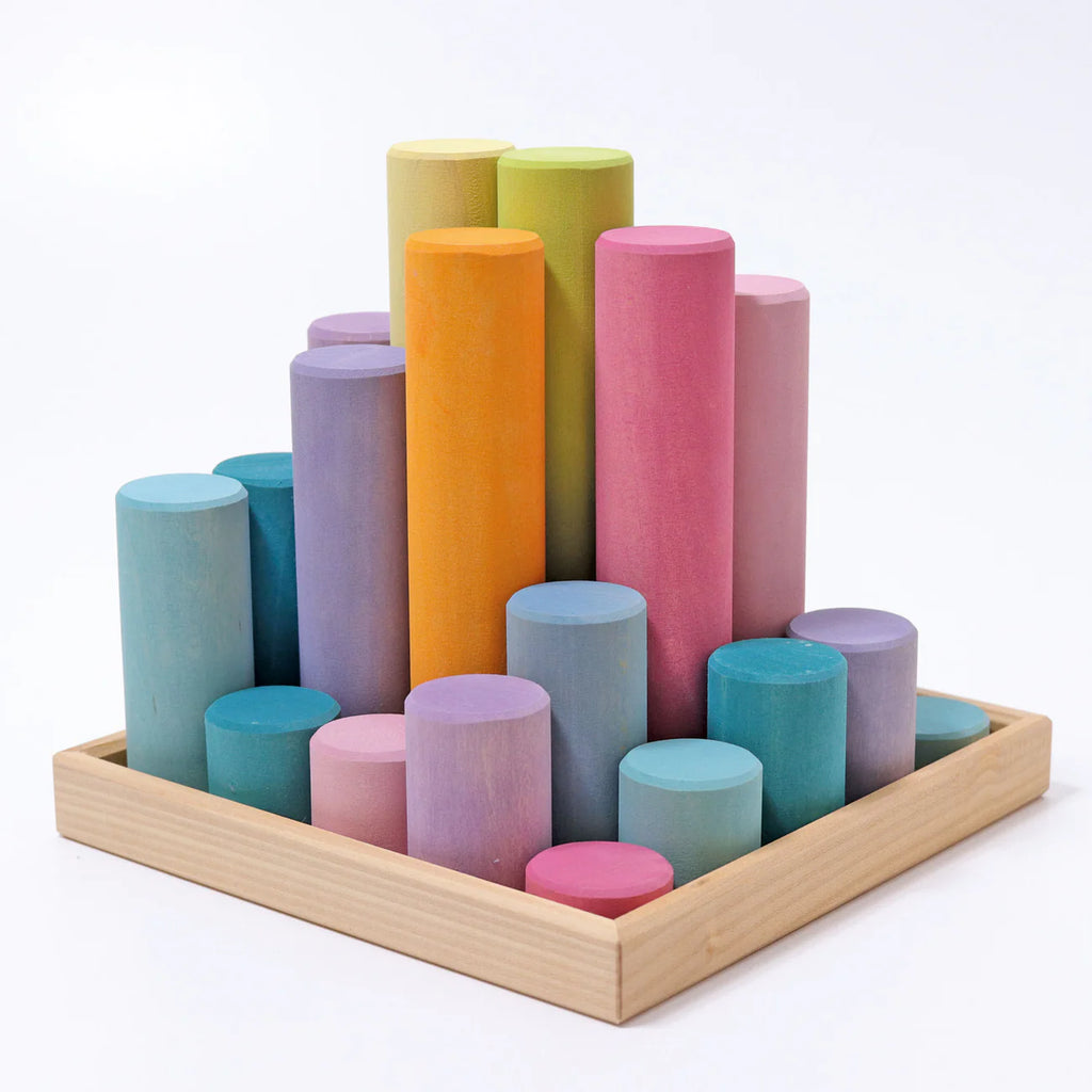Grimm's Large Building Rollers - Pastel (coming soon) features pastel cylindrical blocks of different heights arranged upright in a wooden tray, forming a beautiful gradient stacking game that supports motor skills development.