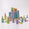 Grimm's Large Building Rollers - Pastel (coming soon) features colorful wooden cylinders, cones, disks, and peg dolls on a light surface with a wooden tray—ideal for stacking games and developing motor skills.