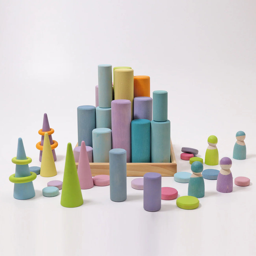 Grimm's Large Building Rollers - Pastel (coming soon) features colorful wooden cylinders, cones, disks, and peg dolls on a light surface with a wooden tray—ideal for stacking games and developing motor skills.