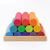Grimm’s Large Building Rollers Rainbow featuring a pyramid of colorful, color-sorting cylindrical wooden blocks stacked in a shallow wooden tray to support motor skills development.