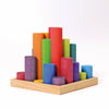 Grimm’s Large Building Rollers Rainbow are colorful wooden cylindrical blocks of varying heights standing upright in a square wooden tray, designed for color sorting and motor skills development.