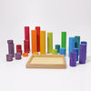 Grimm’s Large Building Rollers Rainbow featuring a wooden tray surrounded by a variety of multicolored cylindrical wooden blocks in different heights and shades, ideal for color sorting and motor skills development.
