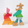 Two abstract figures made from the Grimm's Rainbow Lion Building Set of colorful geometric shapes. The figure on the left consists of red, orange, and pink pieces, while the figure on the right is made up of green, blue, and natural wood tones, forming a playful and imaginative scene.