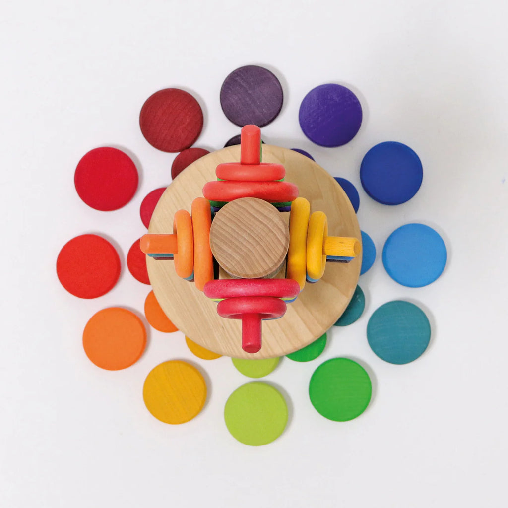 Grimm's Wooden Rainbow Coins (coming soon): Colorful stacking rollers, wooden coins, and rings arranged in a vibrant rainbow pattern, displayed on a white background from an overhead view.