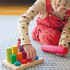 A child playing with a Grimm’s Stacking Game Small Rainbow Rollers wooden board and colorful, cylindrical stacking pieces in a color sorting game.