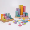Grimm’s Wooden Pastel Coins are artfully arranged on two trays, with extra wooden coins scattered across a white surface.