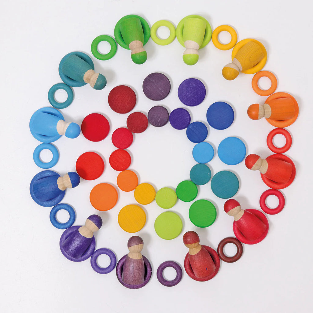 Grimm's Wooden Rainbow Coins (coming soon) are arranged in concentric circles on a white background, creating a rainbow gradient. The coins are organized by color families in a symmetrical, visually striking pattern.