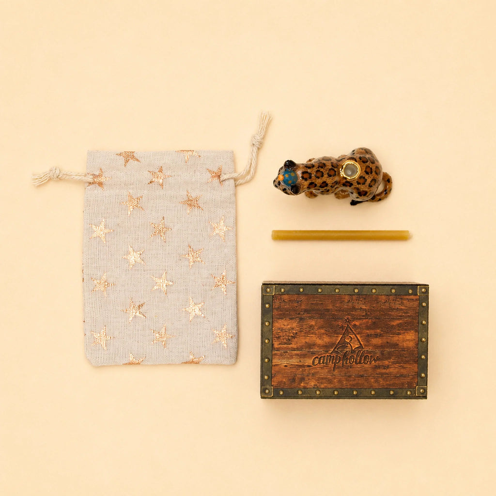 A star-patterned drawstring pouch, the Jaguar Cake Topper - Final Sale (a small handcrafted collectible ceramic jaguar), a yellow stick, and a wooden box with “campholder” on the lid are arranged neatly on a beige background.