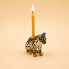 The Jaguar Cake Topper - Final Sale features a hand-painted ceramic jaguar figurine wearing a blue party hat and carrying a lit yellow candle on its back, set against a simple beige background—a delightful birthday decoration that also serves as a collectible keepsake.