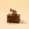 A delightful Jaguar Cake Topper, hand-painted and sporting a blue party hat, perches atop a wooden chest with a star-adorned beige drawstring pouch tucked underneath—making it an irresistible collectible keepsake for birthdays and special celebrations.