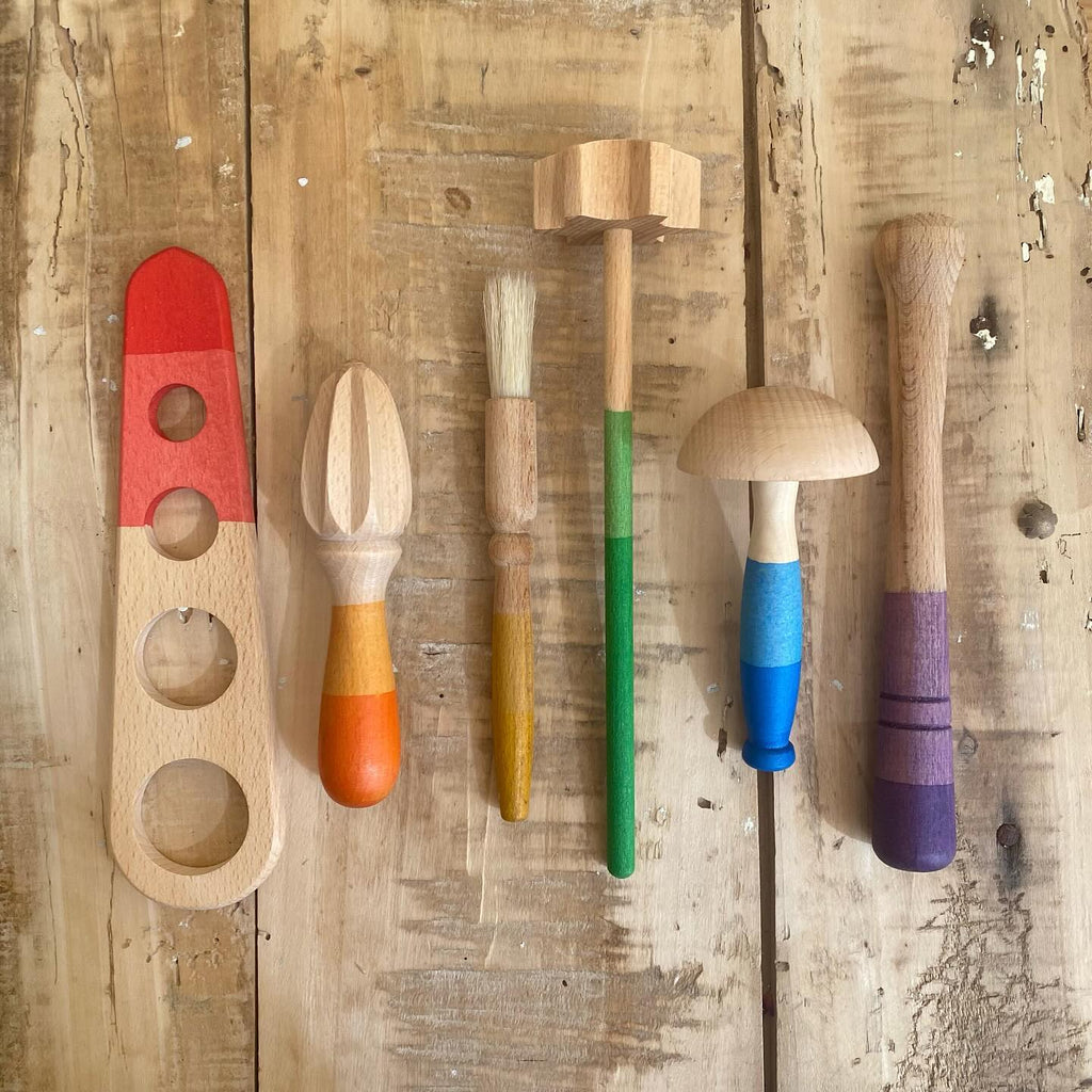 Assortment of Grapat Tools including a red and natural puzzle piece, colorful pegs, a brush, and two mushroom-shaped figures, arranged on an aged wooden background.