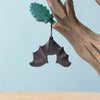 A black wooden bat from a Bumbu Handmade Wooden Halloween Trees With Hanging Bat set hanging from the branch of a spooky tree.