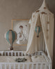 A cozy nursery corner featuring a white crib, cream canopy with gold stars, the Hot Air Balloon - Pastel Green ornament, and a framed child-on-bicycle illustration—ideal for anyone seeking handmade children's room decor.