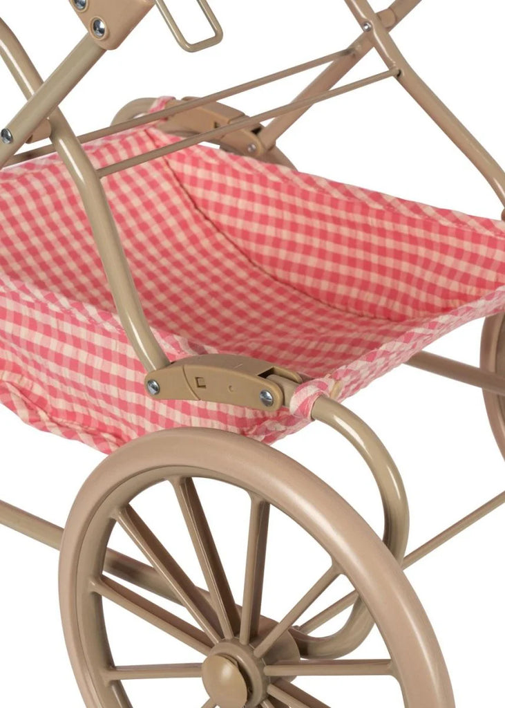 Close-up of the Konges Sloejd Doll Pram - Bubblegum Check, featuring a tan frame with large wheels and a red-and-white checkered fabric basket underneath.