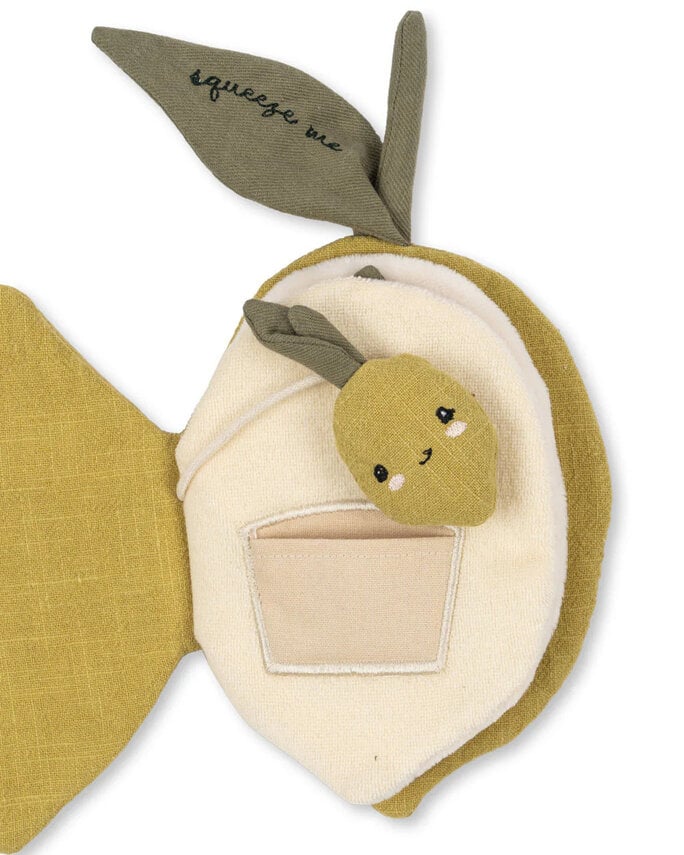 The Konges Sloejd Fabric Lemon Book is a soft, sensory baby book shaped like a lemon with green leaves—one says "squeeze me." It features a smiling plush lemon and a small pocket on a cream-colored background.