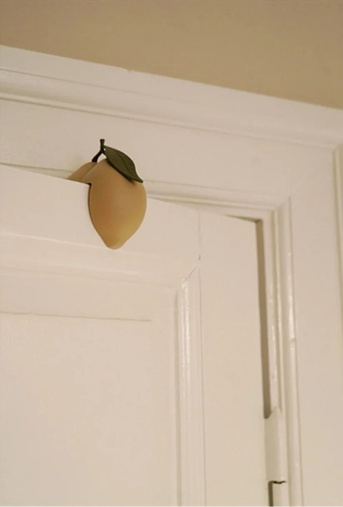 The Konges Sloejd Door Stopper - Lemon, CE-tested and wedge-shaped with a green leaf, props open a white door against its frame.