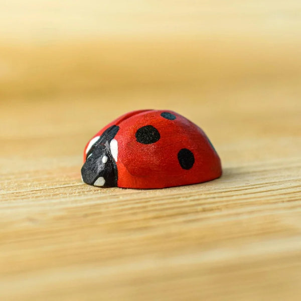 The Bumbu Handmade Wooden Ladybug is a small, handcrafted wooden toy with black spots, resting on a light wood surface and closely resembling a real ladybug.