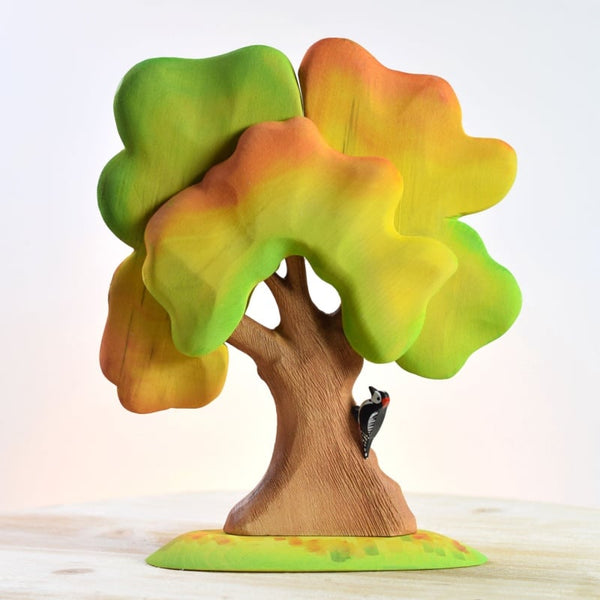 The Bumbu Handmade Wooden Large Oak Autumn and Woodpecker Set is a hand-painted, wooden set with vibrant green, yellow, and orange leaves. Handmade in Romania, it includes a small black woodpecker attached to the trunk.